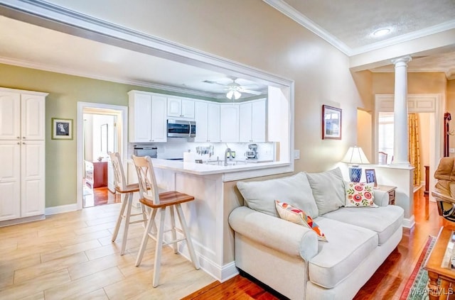 kitchen featuring kitchen peninsula, ornate columns, crown molding, white cabinets, and a breakfast bar area