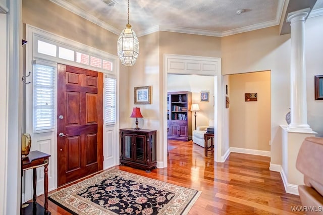 entrance foyer with ornate columns, crown molding, hardwood / wood-style floors, and an inviting chandelier