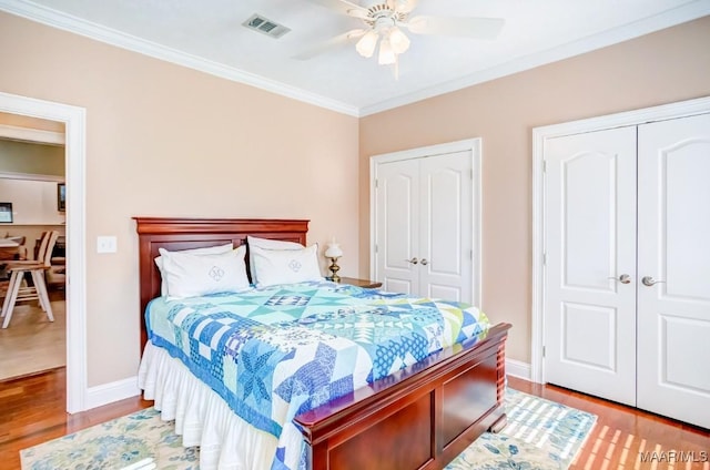 bedroom featuring ceiling fan, ornamental molding, light hardwood / wood-style flooring, and two closets