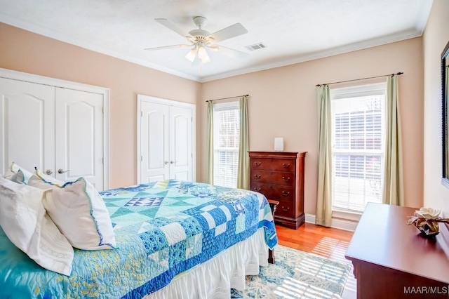 bedroom with ceiling fan, light hardwood / wood-style flooring, crown molding, and two closets