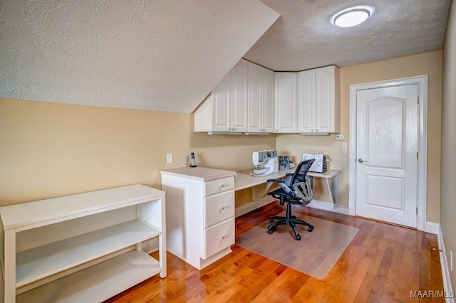 home office featuring a textured ceiling, light wood-type flooring, and built in desk