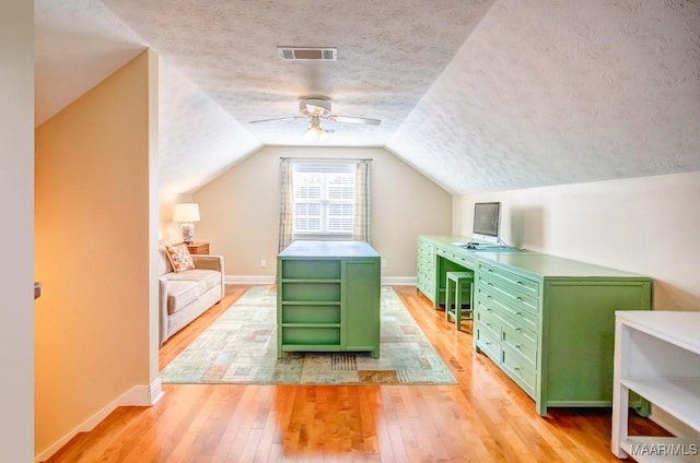 additional living space with a textured ceiling, vaulted ceiling, light hardwood / wood-style flooring, and ceiling fan