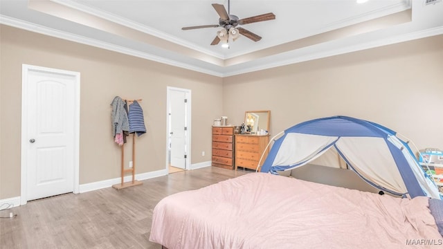 bedroom with light wood-type flooring, a tray ceiling, ceiling fan, and crown molding