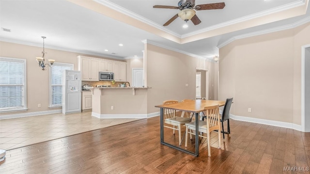 dining room with a tray ceiling, crown molding, ceiling fan with notable chandelier, and light wood-type flooring