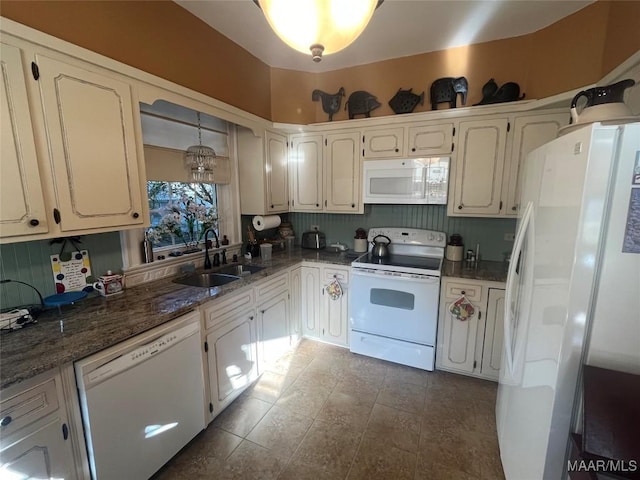 kitchen featuring white appliances, dark stone counters, hanging light fixtures, sink, and a notable chandelier