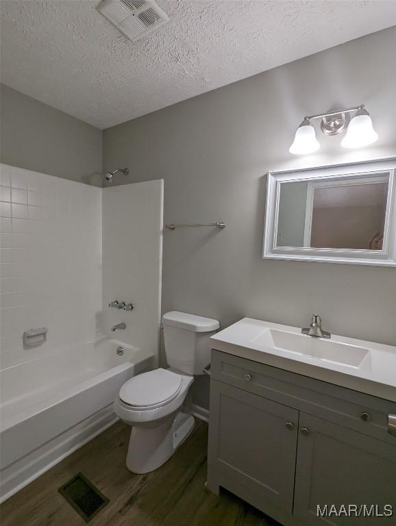 full bathroom with washtub / shower combination, wood-type flooring, a textured ceiling, toilet, and vanity