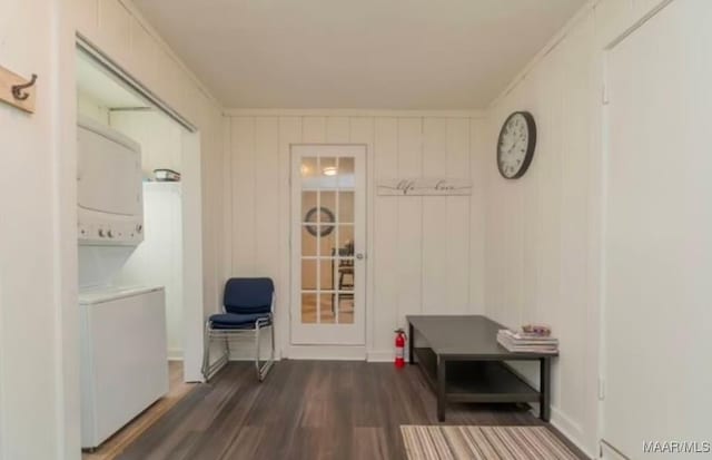 mudroom with wood walls, dark wood-type flooring, stacked washer and clothes dryer, and ornamental molding