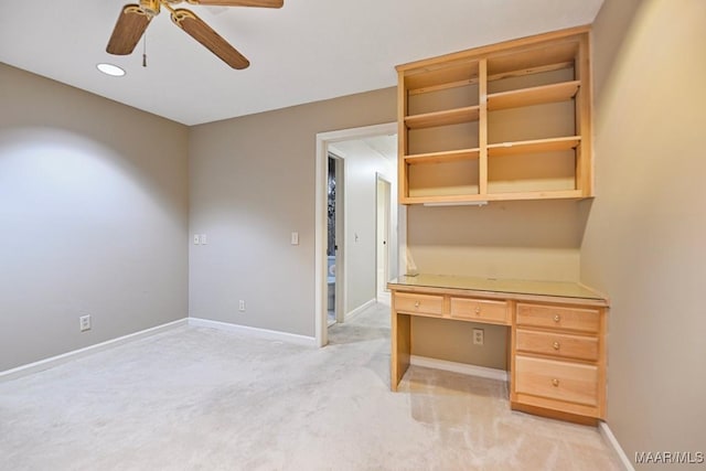 unfurnished office with ceiling fan, built in desk, and light carpet