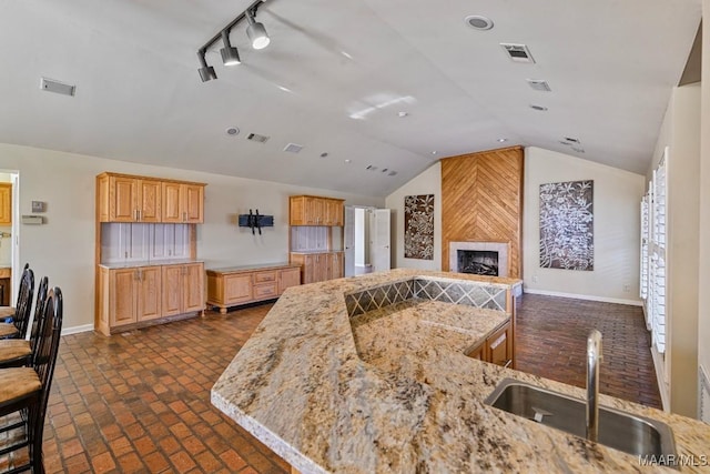 kitchen featuring lofted ceiling, light stone countertops, a premium fireplace, and sink