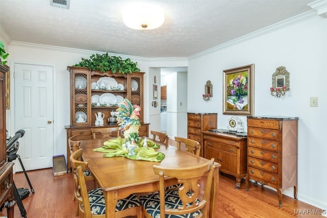 dining area with hardwood / wood-style flooring, ornamental molding, and a textured ceiling