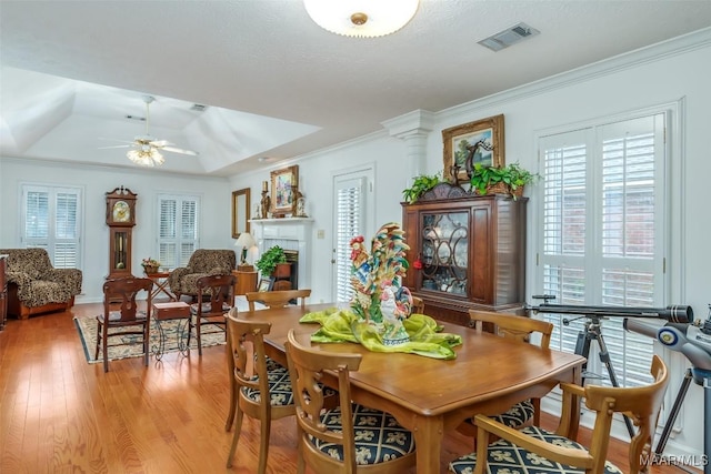 dining area with ceiling fan, a raised ceiling, light hardwood / wood-style floors, a textured ceiling, and ornamental molding