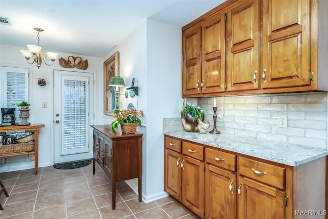 kitchen with decorative backsplash, light stone counters, a chandelier, hanging light fixtures, and light tile patterned flooring