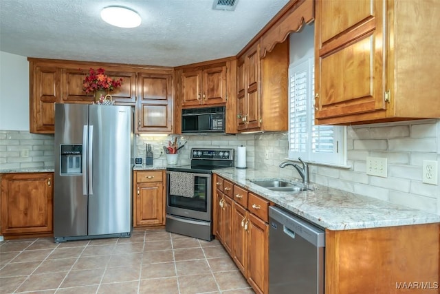 kitchen with sink, light stone counters, a textured ceiling, light tile patterned flooring, and appliances with stainless steel finishes