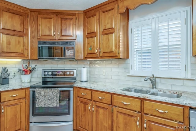 kitchen with appliances with stainless steel finishes, backsplash, light stone counters, and sink