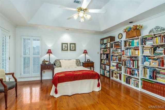 bedroom with wood-type flooring, a raised ceiling, ceiling fan, and crown molding