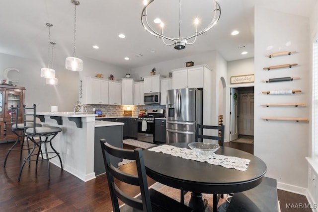 kitchen featuring a kitchen island with sink, decorative light fixtures, decorative backsplash, white cabinets, and appliances with stainless steel finishes