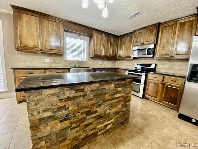 kitchen featuring sink, a center island, a textured ceiling, appliances with stainless steel finishes, and ornamental molding