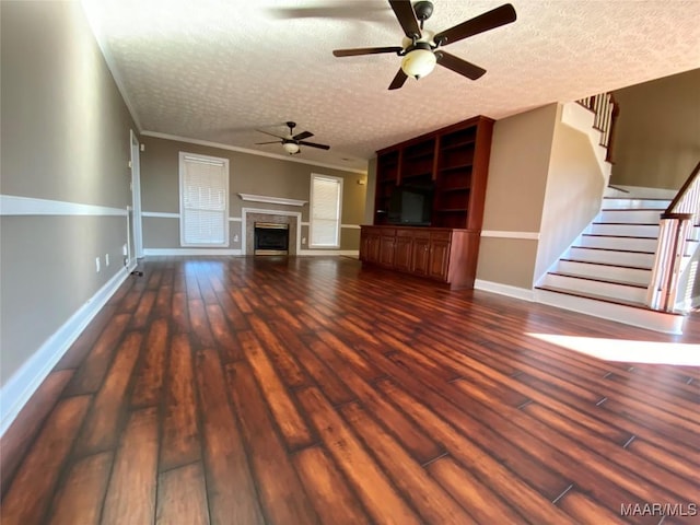 unfurnished living room with a textured ceiling, dark hardwood / wood-style floors, ceiling fan, and ornamental molding