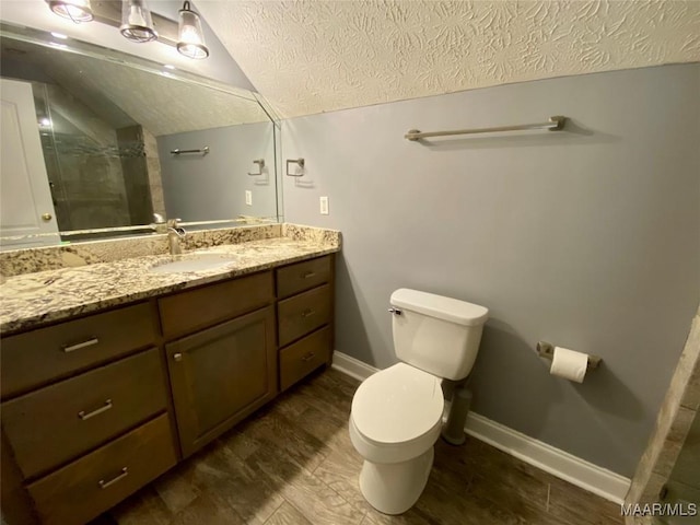 bathroom with vanity, a textured ceiling, vaulted ceiling, toilet, and a shower with shower door