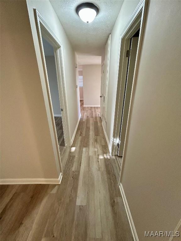 corridor with a textured ceiling and light wood-type flooring