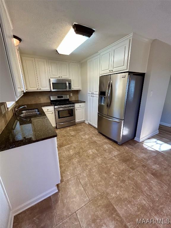 kitchen with appliances with stainless steel finishes, dark stone counters, a textured ceiling, sink, and white cabinets