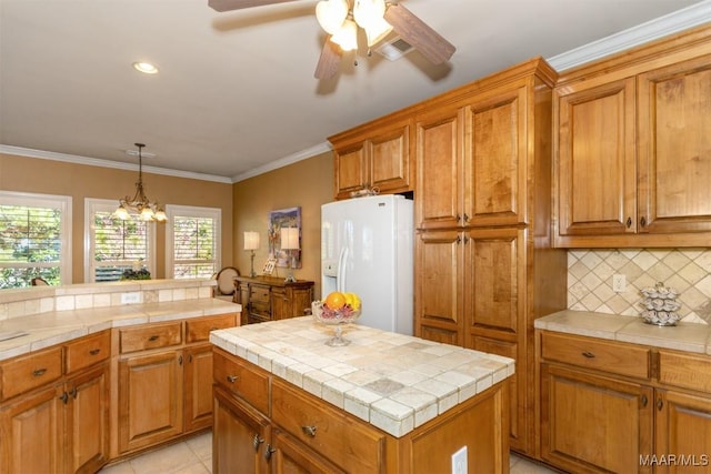 kitchen with a center island, ornamental molding, tile counters, decorative backsplash, and white refrigerator with ice dispenser