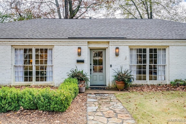 view of exterior entry featuring brick siding and roof with shingles