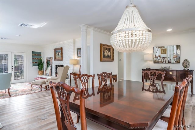 dining room featuring ornamental molding, a brick fireplace, a notable chandelier, and light hardwood / wood-style floors