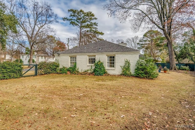 back of house with brick siding, a gate, fence, and a lawn