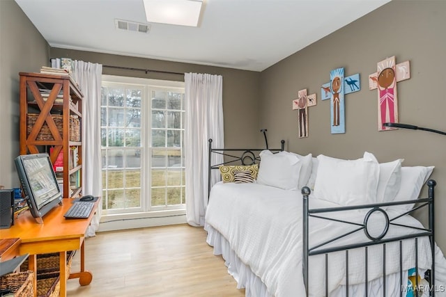 bedroom featuring visible vents, a baseboard heating unit, and wood finished floors