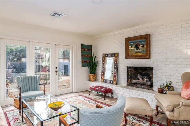 living area with a fireplace, light wood-style flooring, visible vents, brick wall, and french doors