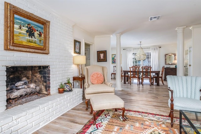living room featuring ornate columns, ornamental molding, visible vents, wood finished floors, and a brick fireplace