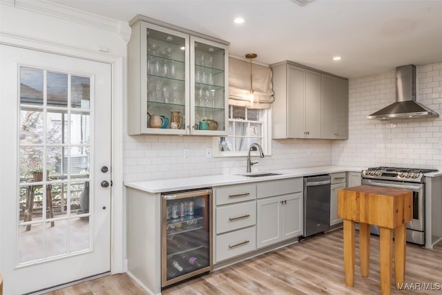 kitchen featuring a sink, wall chimney range hood, light wood-type flooring, stainless steel appliances, and beverage cooler