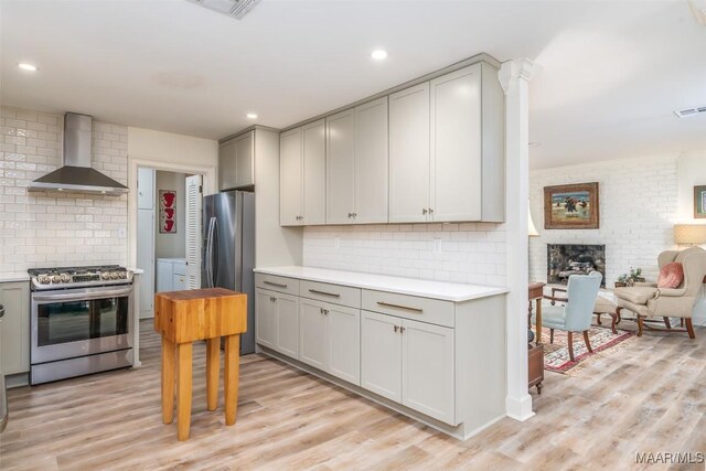 kitchen featuring gray cabinetry, tasteful backsplash, light wood-type flooring, stainless steel appliances, and wall chimney range hood