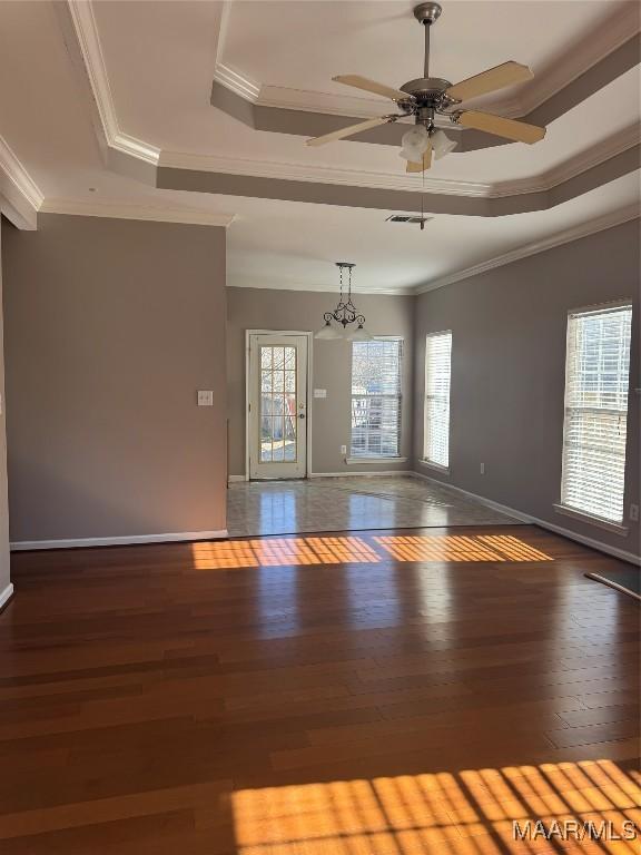 empty room with dark wood-type flooring, a tray ceiling, crown molding, and a healthy amount of sunlight