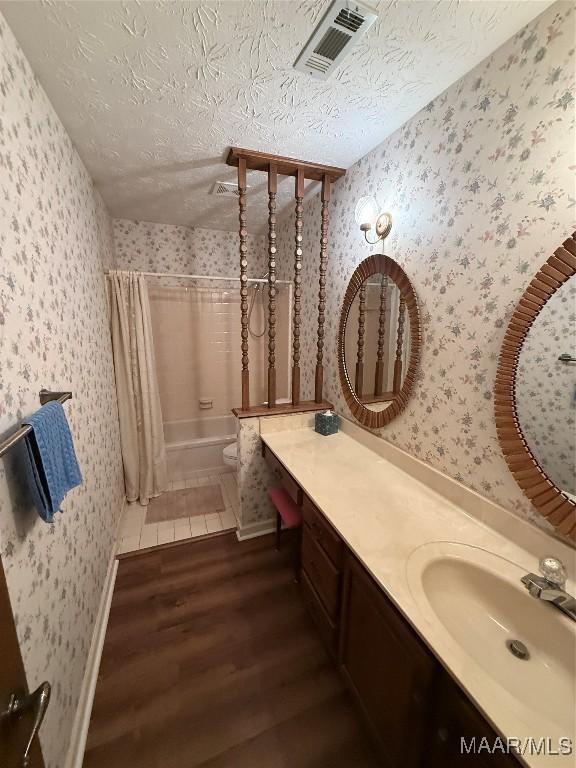 full bathroom with a textured ceiling, shower / bathtub combination with curtain, toilet, wood-type flooring, and vanity