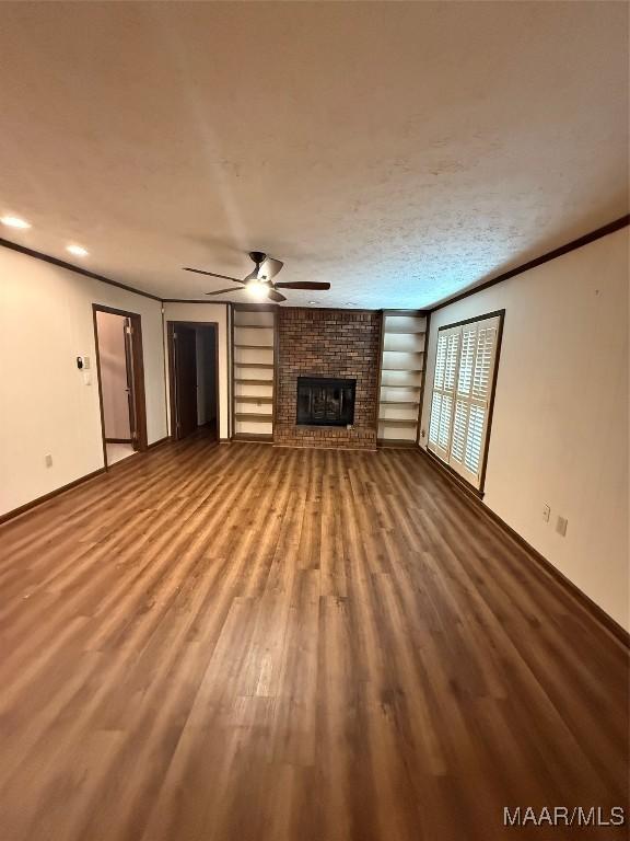 unfurnished living room featuring hardwood / wood-style floors, built in shelves, ornamental molding, ceiling fan, and a fireplace