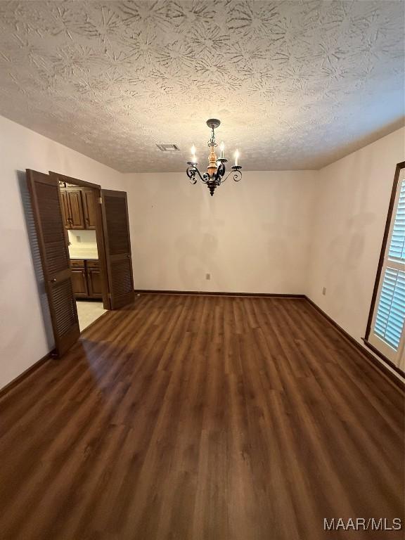 empty room with dark hardwood / wood-style flooring, a textured ceiling, and a chandelier