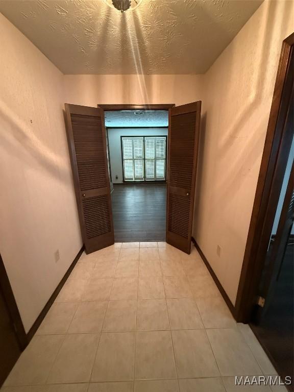 corridor with a textured ceiling and light tile patterned flooring