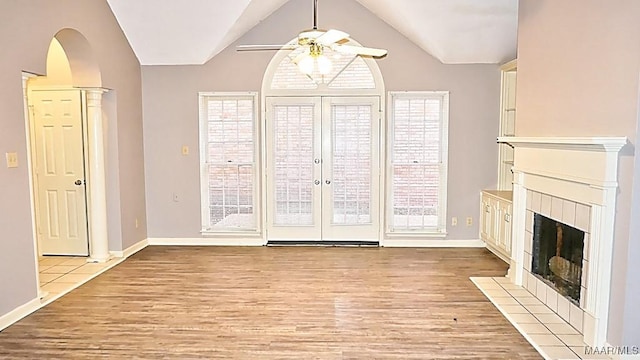 unfurnished living room with light hardwood / wood-style flooring, a tile fireplace, french doors, lofted ceiling, and ceiling fan