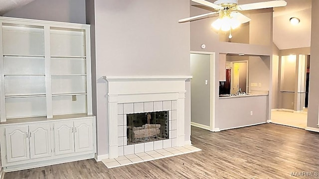 unfurnished living room with lofted ceiling, a tiled fireplace, ceiling fan, and wood-type flooring