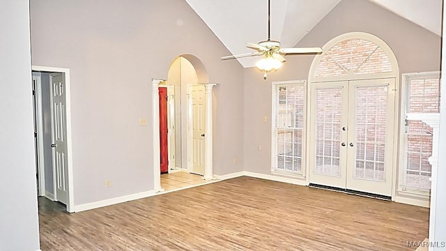 empty room with ceiling fan, light wood-type flooring, french doors, and high vaulted ceiling