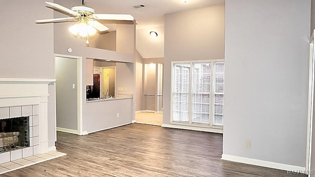 unfurnished living room featuring ceiling fan, a tile fireplace, high vaulted ceiling, and wood-type flooring