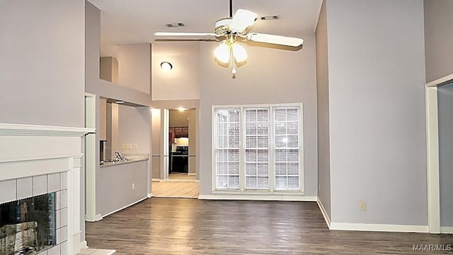 unfurnished living room featuring hardwood / wood-style floors, a high ceiling, a tiled fireplace, and ceiling fan