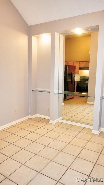 tiled empty room featuring vaulted ceiling