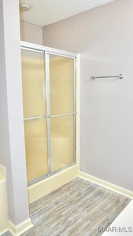 bathroom with a textured ceiling, walk in shower, and hardwood / wood-style floors