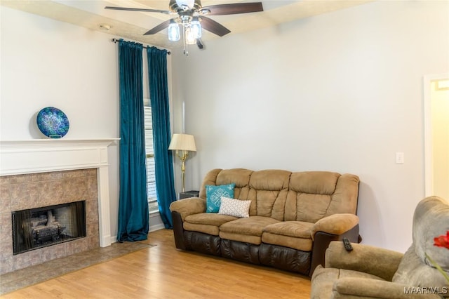 living room with a tile fireplace, ceiling fan, and light hardwood / wood-style flooring