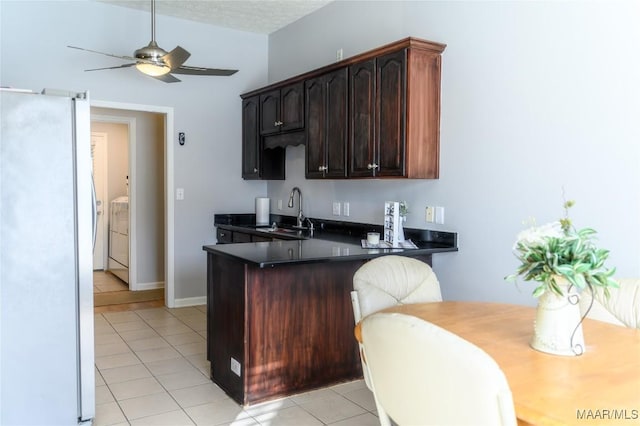 kitchen with sink, stainless steel fridge, dark brown cabinetry, light tile patterned flooring, and separate washer and dryer