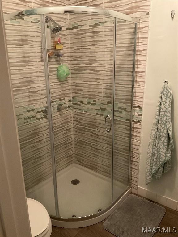 bathroom featuring toilet, a shower with door, and hardwood / wood-style flooring