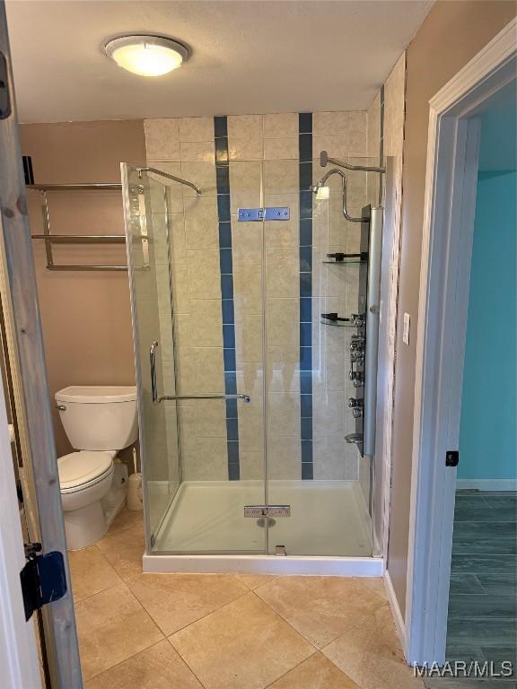 bathroom with toilet, an enclosed shower, and tile patterned flooring